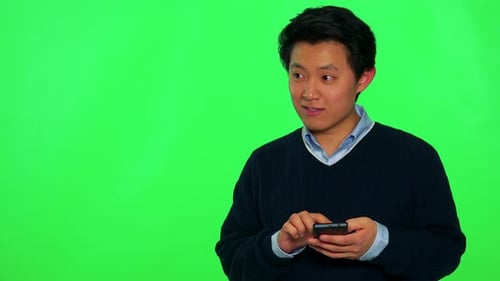 A Young Asian Man Works on a Smartphone with a Smile - Green Screen Studio