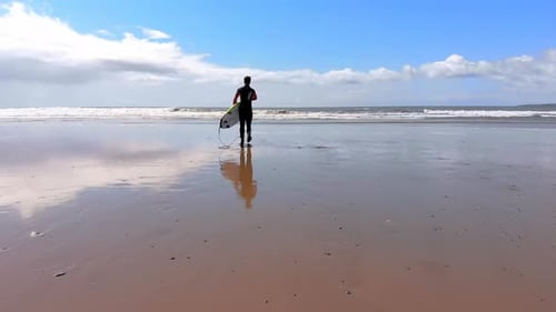 Male surfer walking with surfboard at beach on a sunny day 4k