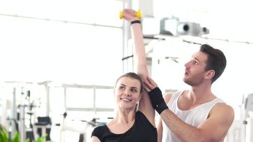 Woman Doing Exercises with Dumbbell on a Gym Background.