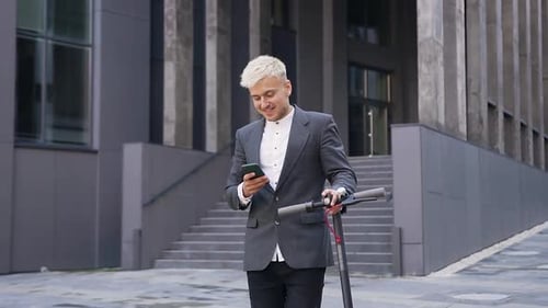 Smiling Man with Scooter Using Smartphone in City