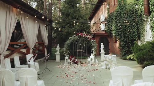 Wedding Arch with Red Flowers and White Chairs Lamp Garland Over the Ceremony Near Restaurant Slow