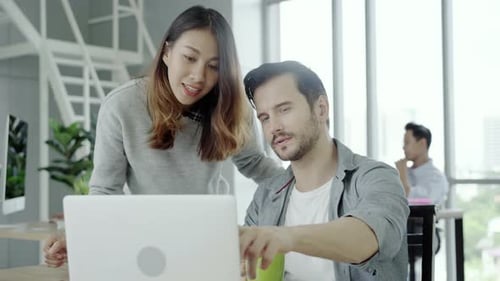 Asian businesswoman giving coffee to her colleague who is working with laptop at office