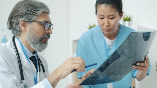 Doctor and Nurse Talking Looking at MRI Brain Scan Discussing Diagnosis in Radiology Clinic