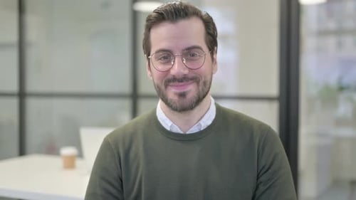 Man with Glasses Waving and Speaking to Camera