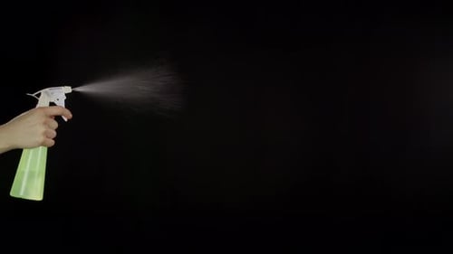 Hand Sprays Liquid from Bottle on Black Background