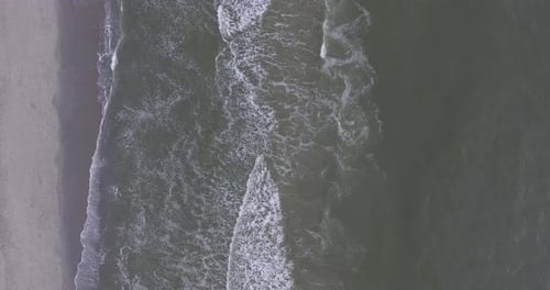 A topdown drone shot by the sea, during sunset, panning back and waves rolling in