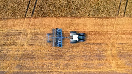 Aerial view of blue tractor plowing field after harvest