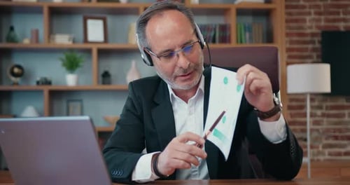Empresario con auriculares y micrófono explicando su historial financiero a sus socios comerciales a través de videochat