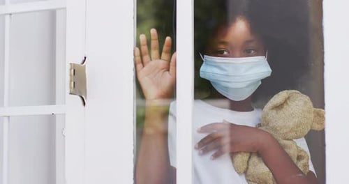 Child With Mask by Window Holding Teddy Bear