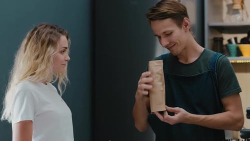 Barista in a coffee shop putting beans in a craft bag and sells it for female customer