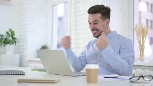 Aufgeregter junger Mann feiert Erfolg auf dem Desktop