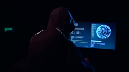 Hooded Figure Working at Computer in Dark Room