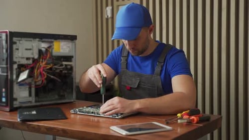 Man Repairs Laptop Computer on Wooden Table
