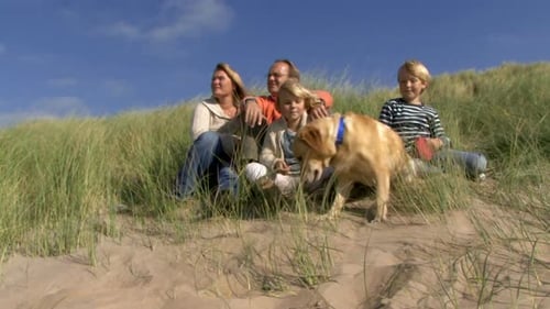 Family Relaxing in Dunes with Labrador Dog