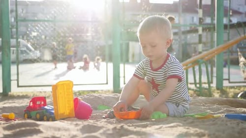 Child Plays in Sandbox with Colorful Toys
