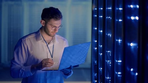 Young Adult Man Uses Laptop in Dark Server Room
