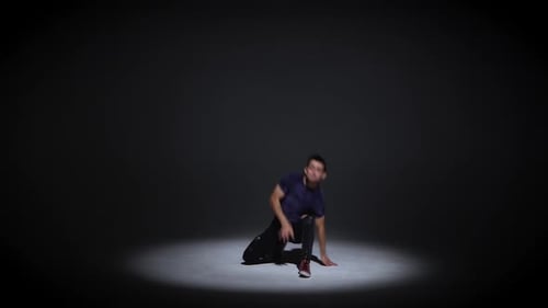 Man tanzt Breakdance auf dunklem Hintergrund in schlichtem grauem T-Shirt und grauen Jeans