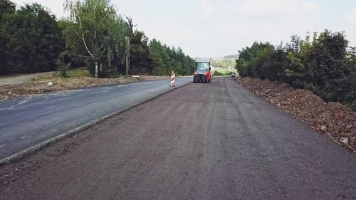 A modern vibratory roller of red color tampers with fresh asphalt on the road