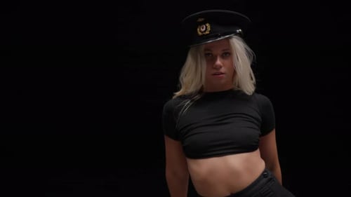 Jeune femme au chapeau de policier danse en studio sur fond noir