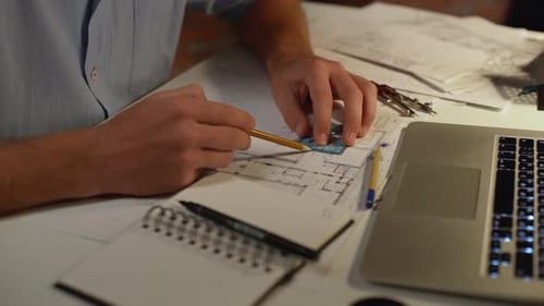 Hands of Caucasian Male in Blue Shirt Drawing with Pencil and Traingle Making Notes at Table with