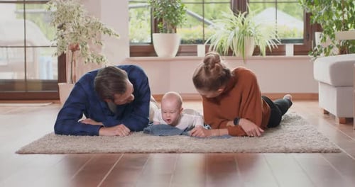 Smiling Young Couple Lying Together on Rug on Their Living Room Floor at Home with Their Adorable