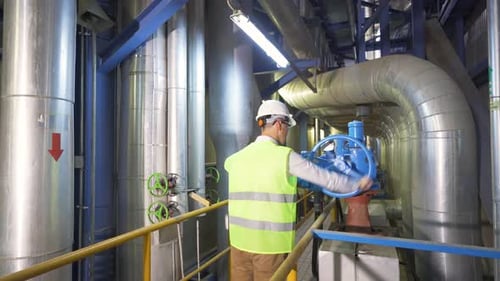 In the industrial factory, the engineer turns the valve.