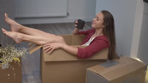 Side View Relaxed Happy Woman Sitting in Box Drinking Tea in Slow Motion Rejoicing Relocation