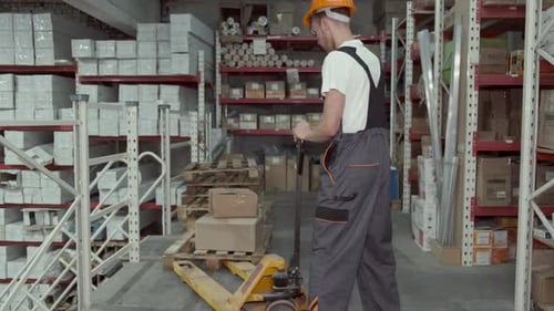 Factory Man Is Loading Cardboard Boxes on a Hand Pallet Truck in Warehouse