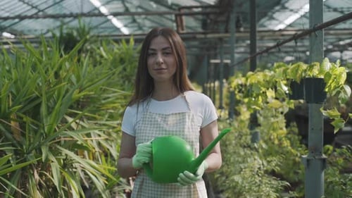 Smiling Woman with Watering Can in Greenhouse