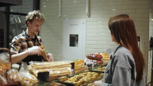 Bread Seller Packing Fresh Baguette for Young Woman Customer in the Beautiful Store with Bakery