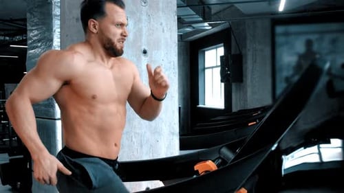 A Bearded Young Man Bodybuilder Running on the Running Track with an Effort in the Modern Gym
