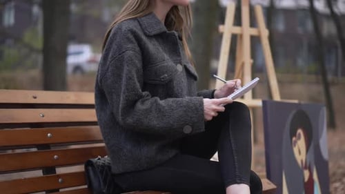 Side View Unrecognizable Thoughtful Woman Drawing Sketch Sitting with Picture on Bench Outdoors