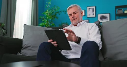 Mature Man Relaxing on Couch Using Tablet