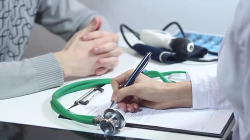 Medical Professional Taking Notes at Desk with Patient