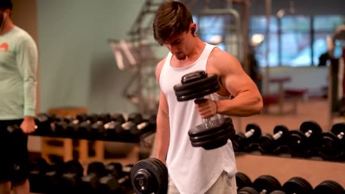 Young Adult Man Lifting Dumbbells at Gym