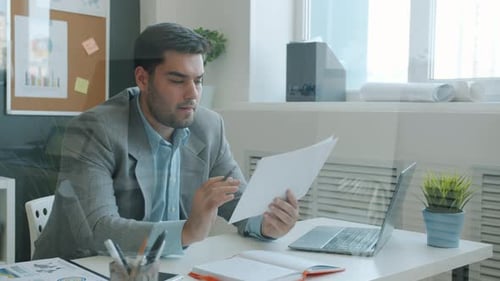 Cámara lenta de un empleado de oficina serio leyendo documentos y tomando notas en la oficina