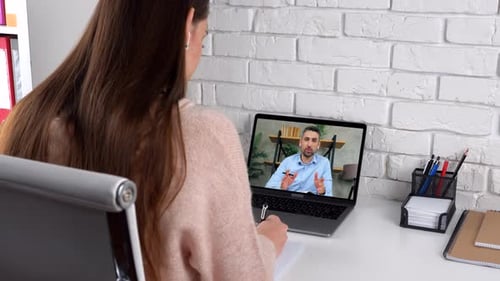 Woman in Virtual Meeting Taking Notes at Desk