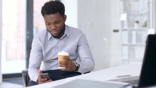 Businessman with Smartphone and Coffee at Office