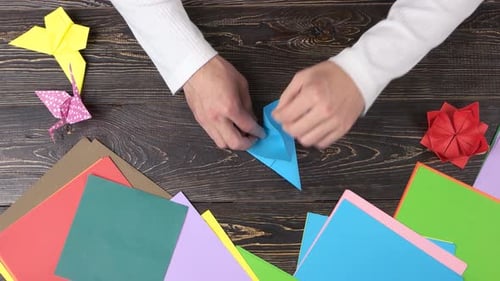 Hände formen blauen Origami-Kranich.