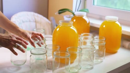 Woman Pours Honey Into Transparent Jars on a White Table