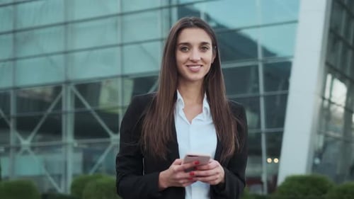 Young Pretty Business Lady Smiling, Girl Stands On The Street With Mobile Phone In Her Hands