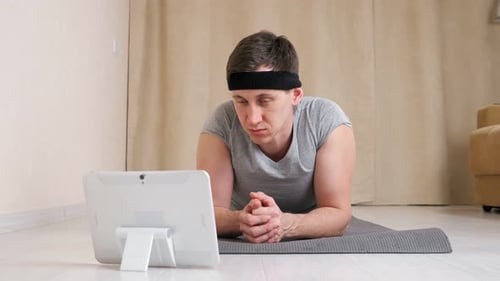 Man Lying on Yoga Mat Looking at Tablet