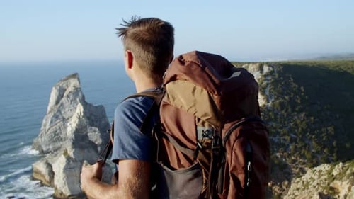 Excited Male Backpacker Standing at Rocky Cliff