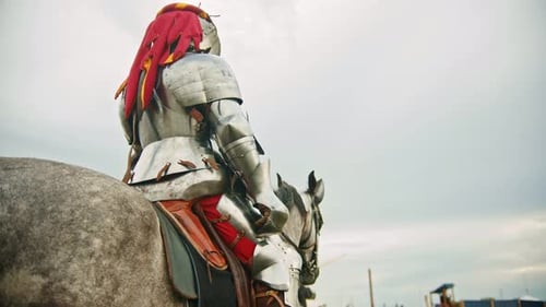 A Man Knight in Helmet with Fabric Clippings Riding a Horse on the Battlefield