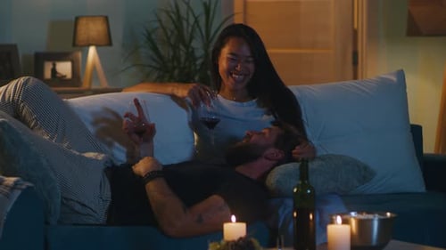 Multiethnic Couple with Wine Chatting on Sofa