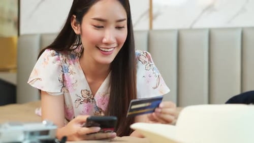 Asian beauty woman plan for trip by mobile and credit card happily on the bed at home.