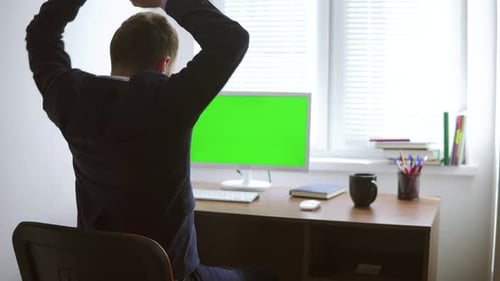 Young Man is Working on a Computer with a Mockup Green Screen at the Table By the Window
