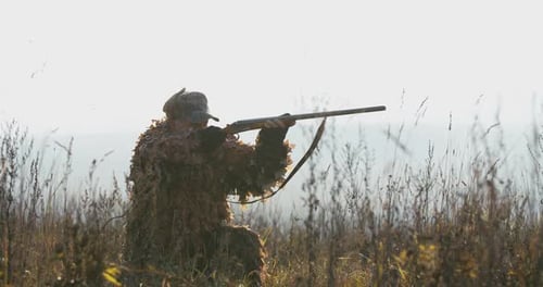 Hunter wartet auf dem Feld. Ein Mann in Jagdausrüstung im Abendlicht findet das Ziel