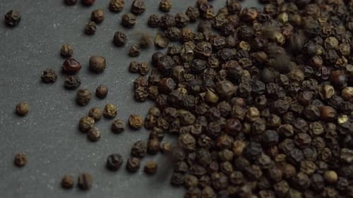 Pile of Black Peppercorns Pouring onto Gray Surface