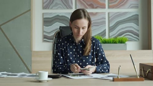 Mujer de negocios con camisa cuenta el dinero sentada en un escritorio de la oficina